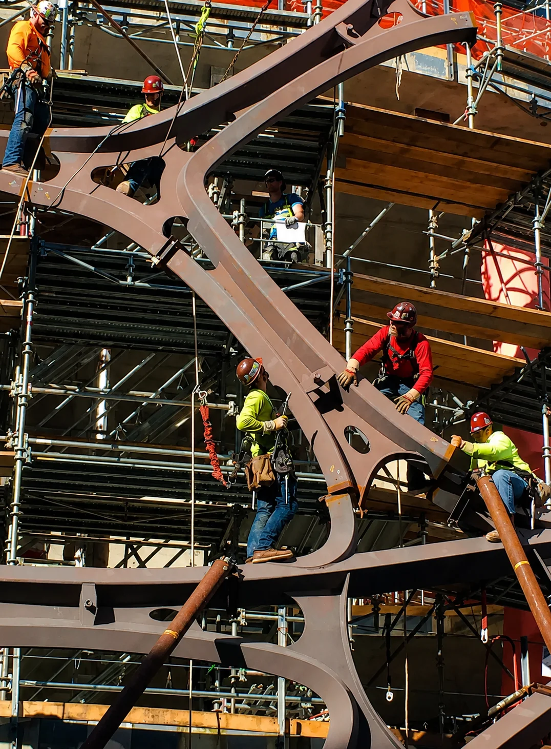 Ironworkers installing structural steel beams on an industrial construction site surrounded by scaffolding