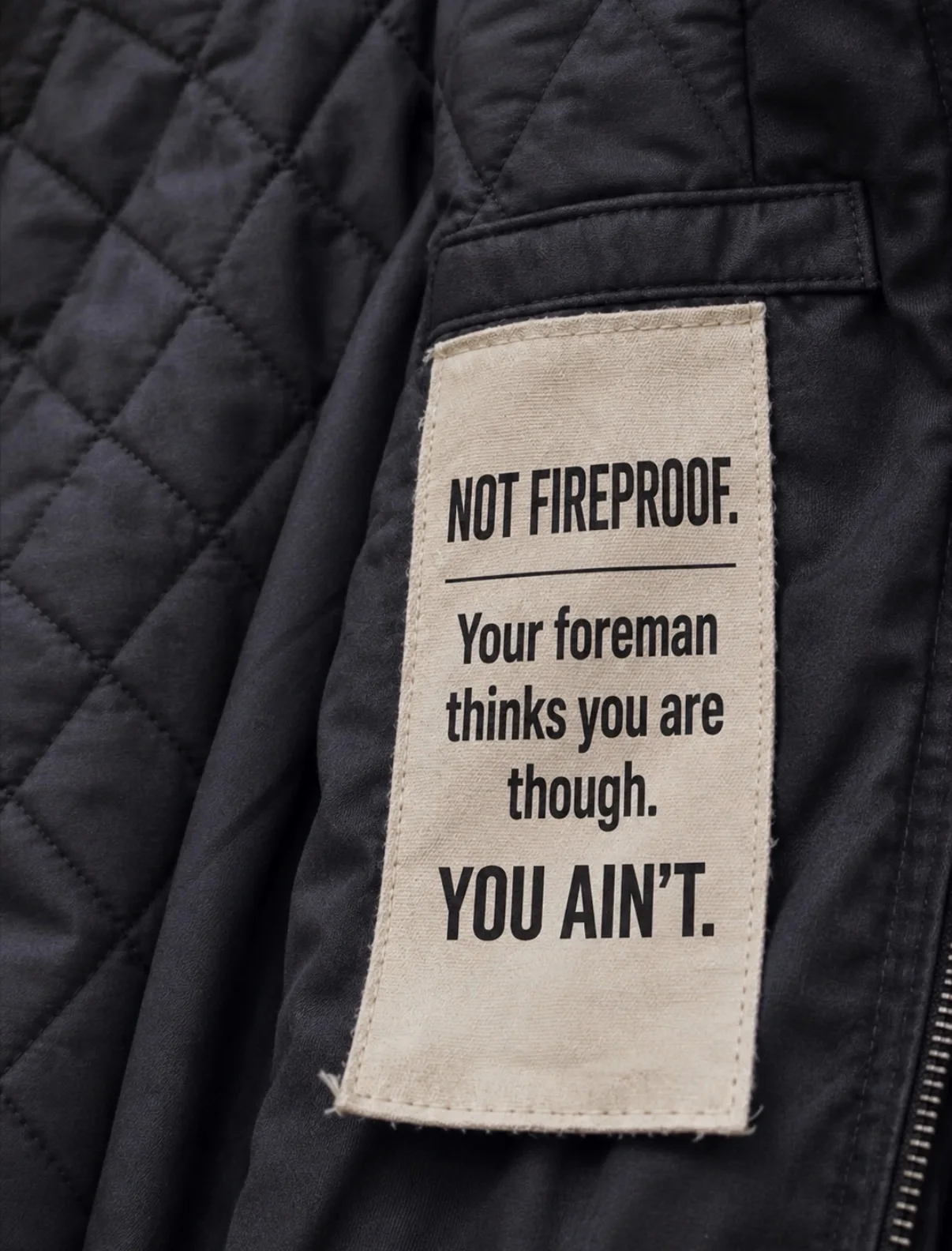 “Not Fireproof” jobsite humor patch on black quilted workwear jacket for welders and industrial tradesmen